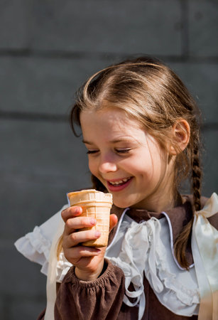 A cute little girl is eating ice cream on a hot summer day. The child is enjoying a sweet dessert during the summer holidays.の写真素材