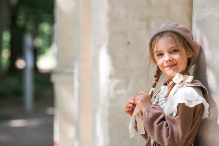 Vintage women's accessories and retro-style clothing. A small, beautiful girl with bows in her hair, in a beige dress and a beret outdoors.の写真素材