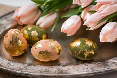 Delicate Easter eggs in pink, golden, and green tones, and delicate pink tulip flowers. The concept...