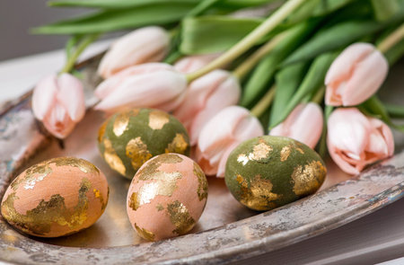 Delicate Easter eggs in pink, golden, and green tones, and delicate pink tulip flowers. The concept...