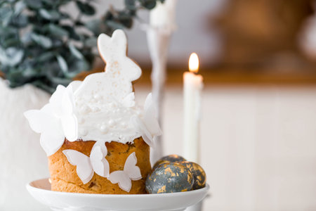 Happy Easter 2026. Easter cake with a white rabbit and butterflies, gilded Easter eggs, candles, and...
