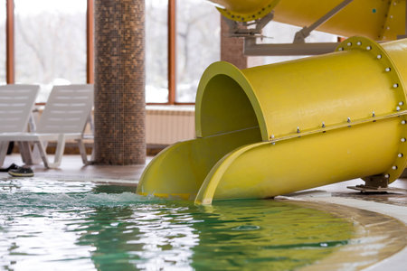 Yellow slide in an indoor pool with sun loungers and clear turquoise water. Water park for children.