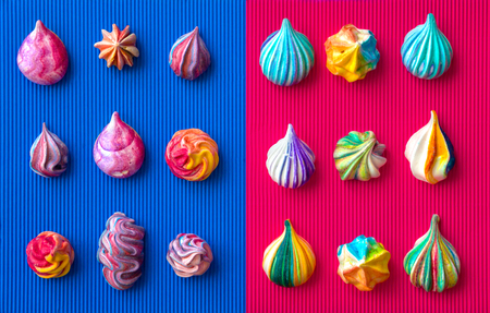 Small multicolored meringue cakes on a combination of two colors background. Bright blue and purple corrugated background. Appetizing meringues. View from above.の写真素材