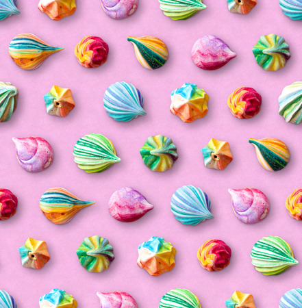 Seamless pattern of multicolored meringues. Colorful little meringue cakes on a pink pastel background. Appetizing meringues. Arrangement of cakes in several rows. View from above.の写真素材