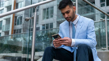 Middle Eastern businessman sitting on stairs touching mobile phoneの写真素材