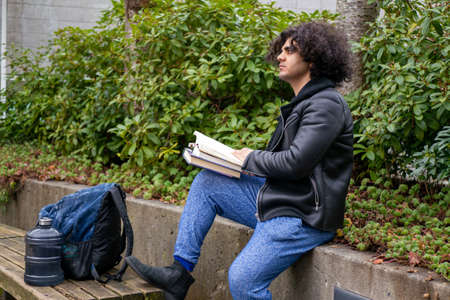 A man and a college student reading a book near a treeの写真素材