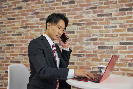 Businessman making phone calls while touching laptop in suitの写真素材