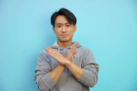 Asian man making a bat in front of blue backgroundの写真素材