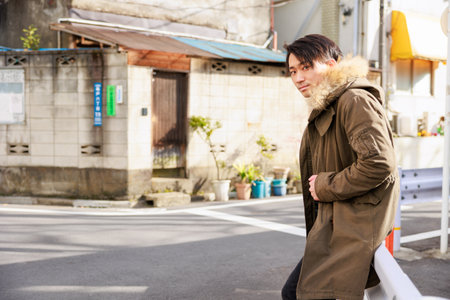 Young man in winter jacket standing on the street, looking at cameraの写真素材