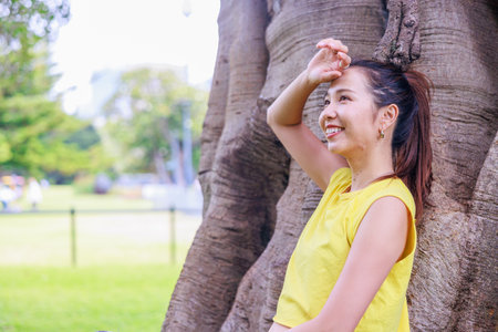 Beautiful asian woman in yellow t-shirt standing under the treeの写真素材