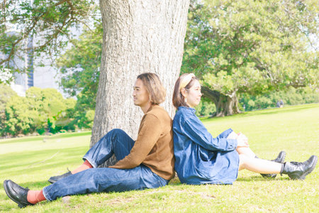 Young couple sitting on the grass in the park with trees in the backgroundの写真素材