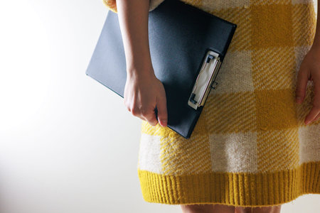 Woman in a yellow sweater holding a notebook and a stapler