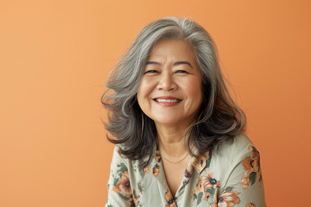 Portrait of a happy senior asian woman smiling against orange backgroundの素材