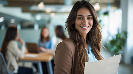 Portrait of smiling businesswoman holding papers while colleagues working in background at officeの素材