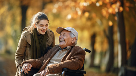 Smiling senior man in wheelchair with young caregiver in autumn parkの素材