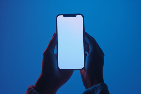 Mobile phone with white screen in female hands on a blue background.の素材