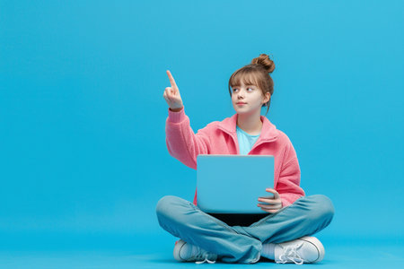 Young woman sitting on the floor and using laptop computer on blue backgroundの素材