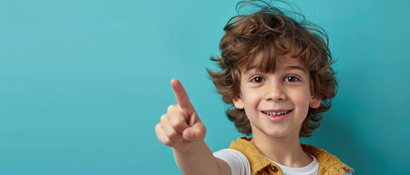 Little boy with curly hair on a blue background points his finger at the cameraの素材
