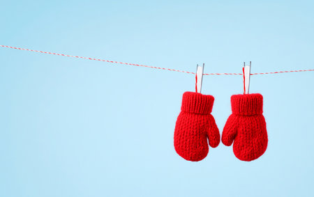 Red knitted mittens hanging on a clothesline on a blue backgroundの写真素材