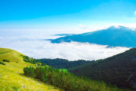 Alpin view to a valley above clouds. Apennines mountains in summer. Green grass and forest, mountain...