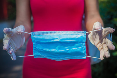 Light blue medical mask demonstration. Hands in white gloves. Female silhouette in red dress out of...