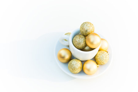 top view of coffee cup with golden Christmas balls inside and around. Coffee pair on white surface....