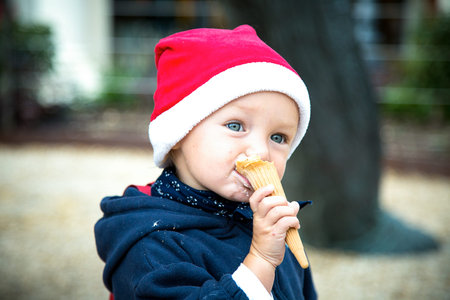 Blue eye baby girl in dark blue winter coat and red Christmas hat eats ice-cream in waffle cone....