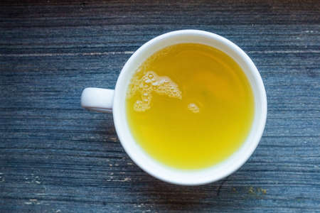 White round porcelain tea cup with fresh herbal green tea. Hot healthy beverage for breakfast. Wooden background. top view geometrical composition. Vitamine cocktail. Raw biological vegan beverageの写真素材