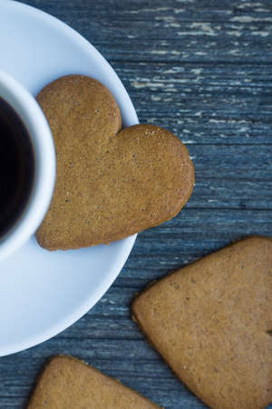 Vertical picture of gingerbread heart shaped biscuit on white porcelain plate. Coffee break with love. Side of coffee cup with hot beverage. Homemade sweets. Postcard and wallpaper picture. traditionの写真素材