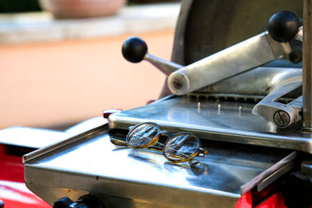 Slicing machine with eyeglasses. Spectacles on metal mechanical grocery knife. Vintage shop equipment. Calm reflection concept. Food supply. Closed for summer. Metal machine.の写真素材