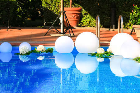 Open air swimming pool decorated with white floating balls and fresh flowers for wedding party. Summer event preparation. Party design. Clean transparent blue water. Background and postcard pictureの写真素材