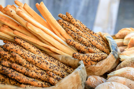 many fresh bread sticks with salt and seeds in paper bags and other bakery around. degustation of bread. Catering and finger food. Wallpaper and postcard picture. Nutrition concept. Gluten product.の写真素材
