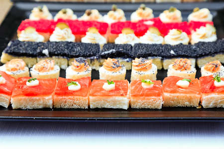 Many small colourful sandwiches with fish, red and black caviar. Fingerfood with seafood. Sushi like tiny snacks for wedding. Background. Menu picture. Catering food. Delicious canapes in restaurantの写真素材