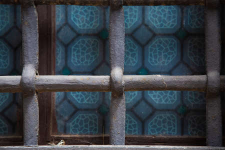 Metal grey ancient grate on the window with blue stained glass. Medieval protection from thieves. Construction sample. Background and wallpaper picture. Geometrical square composition. Protectionの写真素材
