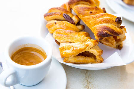 Traditional italian breakfast. Small white cup of hot caffe ristretto and two fresh croissant with apple and nuts. Good morning concept. Daylight. Homemade bakery. Ginseng hot drink and apple pieの写真素材