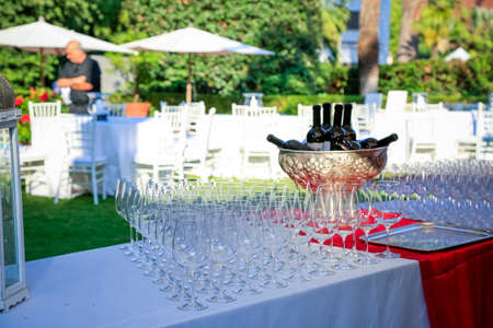 many crystal wineglasses and red wine in a metal vase on buffet table in garden. Blurred background. Wine tasting preparation. Wedding party decoration. Restaurant outdoors, Catering service.の写真素材