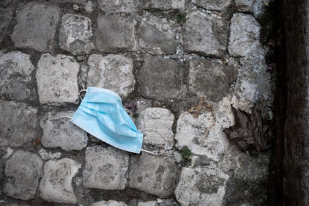 Horizontal picture. Used blue medical mast FFTP-2 frown away on grey cobblestone pavement. Black and white with blue. Contrast picture. Pollution concept. Coronavirus. Ecology and recycling.の写真素材