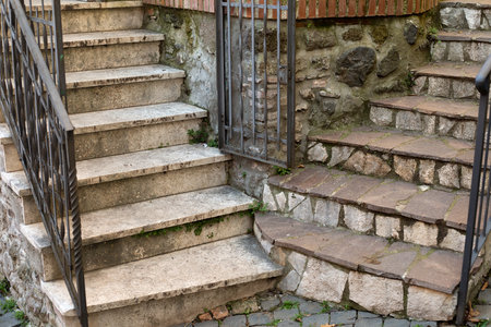 Two stone staircases with metal forged railing and a gate in the corner of old medieval house. Italian old town architectural element. Marble steps. Grey outdoor ladder.の写真素材