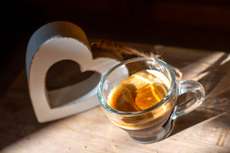 Top view to transparent coffee cup of italian espresso with wooden heart behind. High contrast morning Kitchen photo. Background blurred. Homemade breakfast. Coffee lovers concept. Wallpaper pictureの写真素材