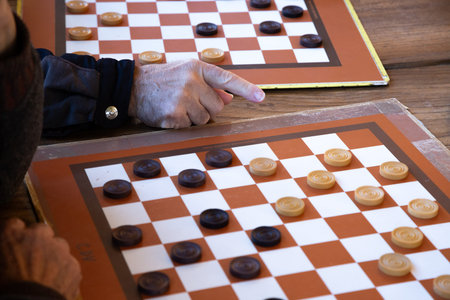 A person is engaged in a game of checkers on a wooden table surface