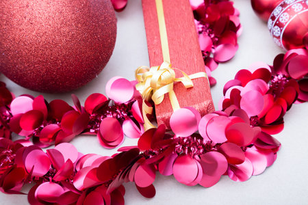 A red gift box with a gold bow amid red Christmas decorationsの写真素材