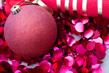 A vibrant red Christmas ornament is beautifully surrounded by red confettiの写真素材
