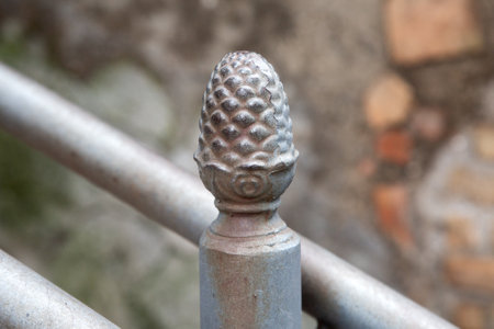 This is a detailed close up of a shiny metal pole topped with a pine coneの写真素材