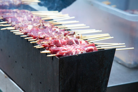 A long row of delicious meat on sticks is cooking on a grillの写真素材
