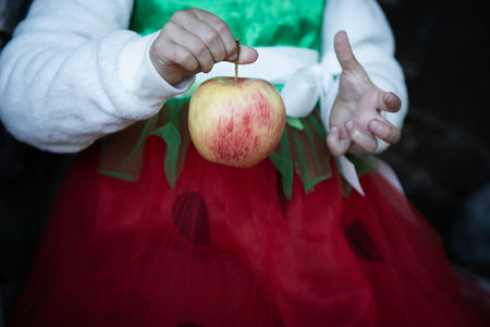 A girl in a red and green outfit holds an apple in her handの写真素材