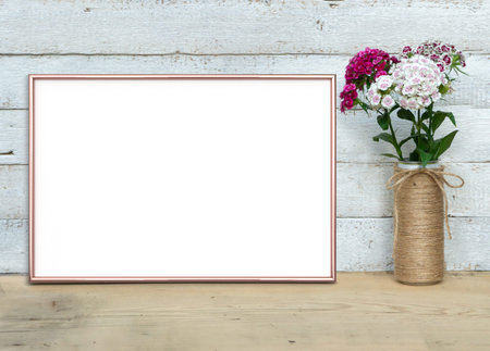 Rose Gold horizontal A4 Frame mockup near a bouquet of sweet-william stands on a wooden table on a...