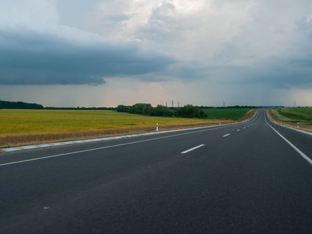 Asphalt road through the fields and meadows with cloudy sky.の写真素材
