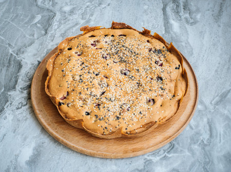 Homemade cherry tart sprinkled with sesame seeds on a round cutting board on a marble topの写真素材