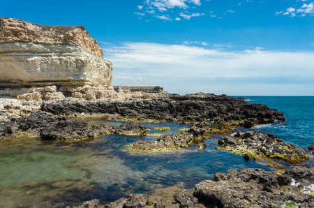 High cliff of limestone on the sea coast against a background of blue sky with cloudsの写真素材