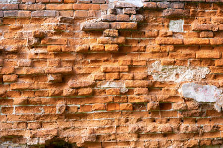 An old brick wall with bricks that are badly deteriorating from time and external influencesの写真素材